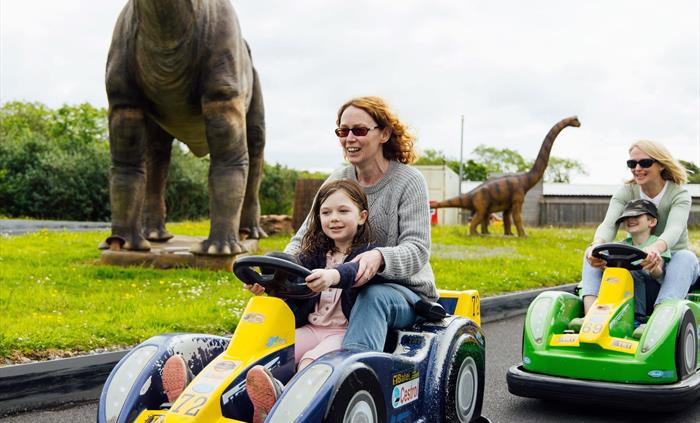 Two mums with their children, each on a go-kart, racing each other on the race track.